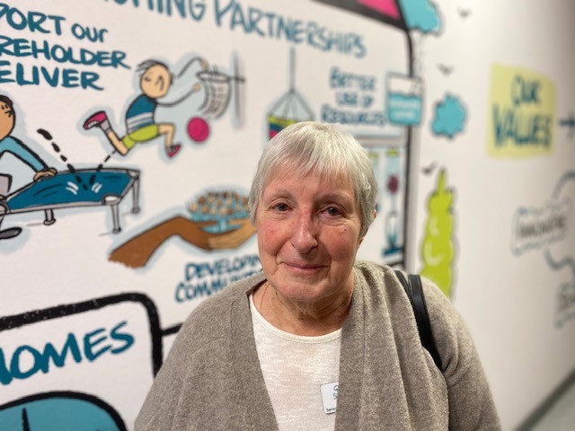 Involved Customer, Ros, standing in front of the Homes in Somerset Corporate Strategy wall art in the office space.